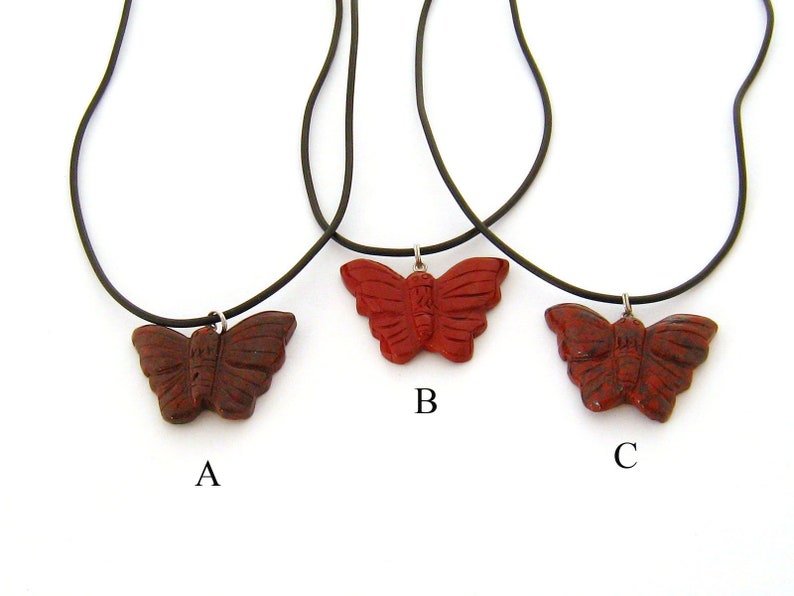 May include: Three red butterfly necklaces with black cords. The butterflies are carved from red jasper and have a detailed design. The necklaces are labeled A, B, and C.