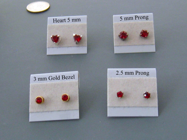 May include: Four cards with red gemstone earrings on white cardstock. The cards are labeled with the earring style and size: Heart 5 mm, 5 mm Prong, 3 mm Gold Bezel, and 2.5 mm Prong.