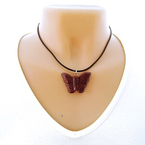 May include: A dark brown wooden butterfly pendant necklace on a black cord.