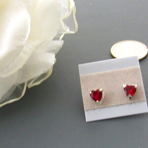 May include: A pair of silver heart-shaped stud earrings with red gemstones.