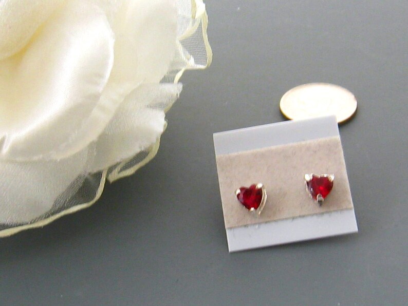 May include: A pair of silver heart-shaped stud earrings with red gemstones.