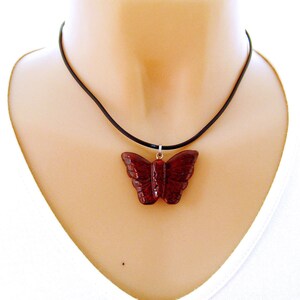 May include: A red butterfly pendant necklace on a black cord. The pendant is carved from a dark red stone and has a detailed design.