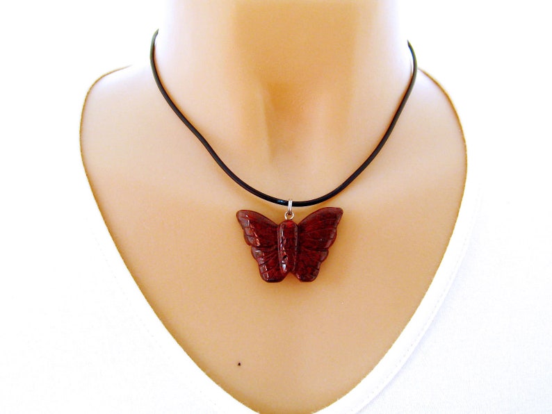 May include: A red butterfly pendant necklace on a black cord. The pendant is carved from a dark red stone and has a detailed design.