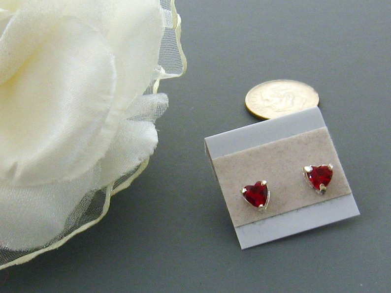 May include: A pair of silver heart-shaped earrings with red gemstones. The earrings are displayed on a white card with a brown backing.