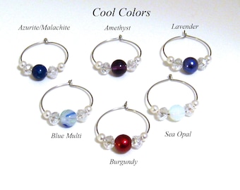 May include: A collection of six silver hoop earrings, each featuring a central gemstone in various cool colors, including blue, purple, and red. The earrings are accented with small pearls and clear crystal beads. The text "Cool Colors" is at the top.