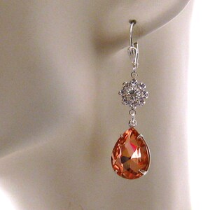 May include: Silver dangle earrings with a teardrop-shaped orange crystal and a cluster of smaller clear crystals.
