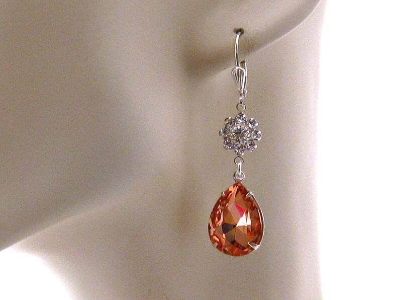 May include: Silver dangle earrings with a teardrop-shaped orange crystal and a cluster of smaller clear crystals.