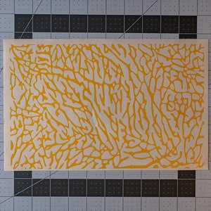 May include: A yellow stencil with a camouflage pattern. The pattern is made up of irregular shapes and lines.