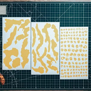 May include: A selection of yellow and white stickers, featuring irregular shapes and small circles, are laid out on a black cutting mat. A black handgun, a knife, and a roll of tape are also present.