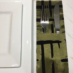 May include: A table setting featuring a white rectangular plate, a silver fork and knife, and a green and black patterned napkin. The napkin is folded to hold the cutlery.