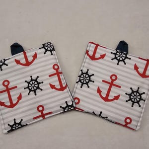 May include: Two square nautical-themed pot holders. Each pot holder features a white background with gray horizontal stripes and a pattern of red anchors and black ship wheels. A navy blue loop is sewn on the top corner of each pot holder.