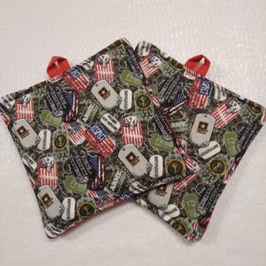 May include: Three square pot holders with red trim and hanging loops. The fabric features a camouflage pattern with American flags, dog tags, and the word "ARMY". The pot holders are designed for kitchen use.