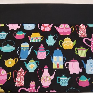 May include: Black fabric with a repeating pattern of colorful teapots in various designs. The teapots are pink, blue, yellow, and green, with floral and geometric patterns. The background is black.