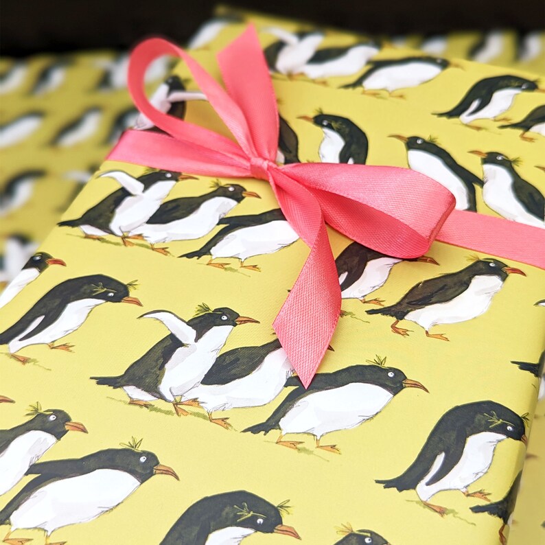 Puede incluir: Papel de regalo amarillo con un patr&oacute;n repetitivo de ping&uuml;inos negros y blancos. Una cinta rosa est&aacute; atada alrededor del papel en forma de lazo.
