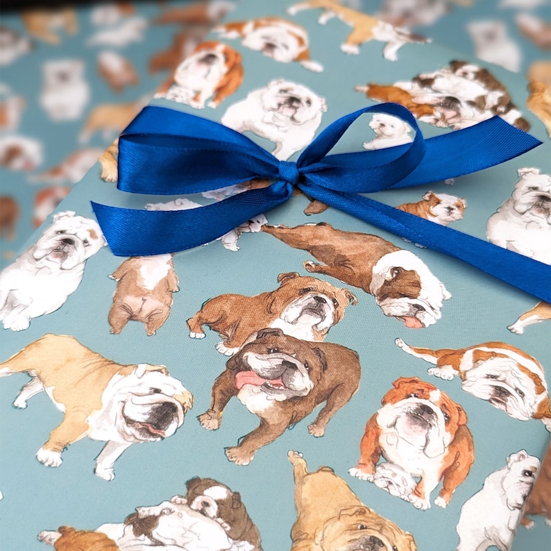 May include: Blue and white wrapping paper with a repeating pattern of bulldog illustrations. A blue ribbon is tied around the paper.