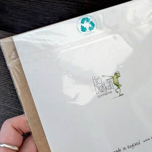 May include: A white card with a green frog illustration and the text "Hes Durkan Illustration" printed on it. The card is packaged in a clear plastic sleeve and has a green and blue circular sticker with a recycling symbol and the text "Compostable & Biodegradable Packaging" printed on it.