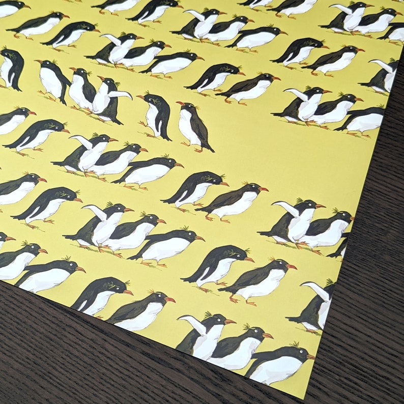 Puede incluir: Un papel de regalo amarillo con un patr&oacute;n repetitivo de ping&uuml;inos negros y blancos. Los ping&uuml;inos miran en diferentes direcciones y algunos est&aacute;n de pie mientras que otros nadan.