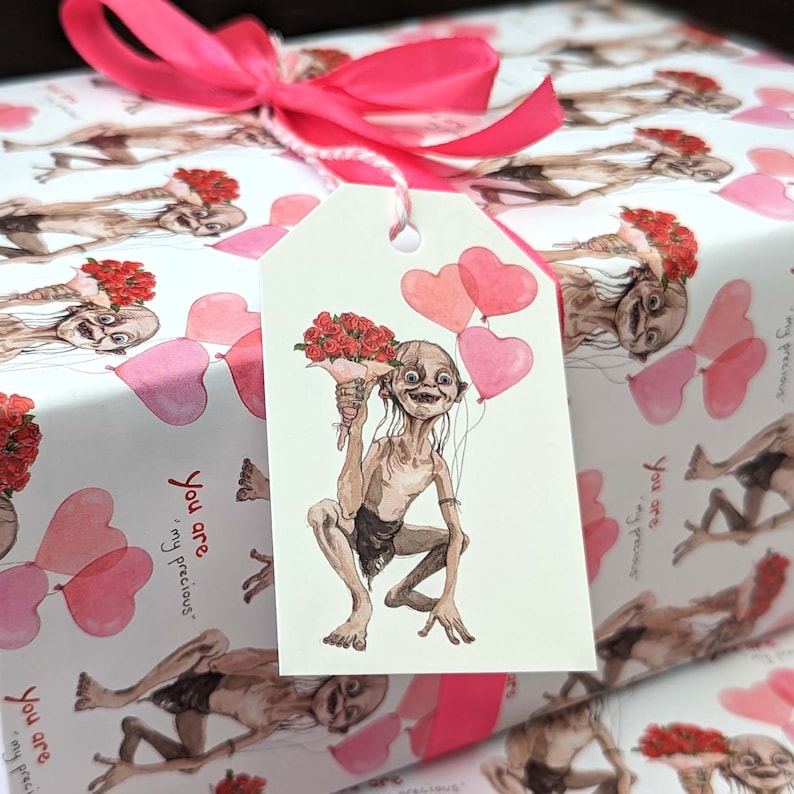 May include: Gift wrap with a repeating pattern of a character holding flowers and heart-shaped balloons. A gift tag with the same character and balloons is tied with a pink ribbon. The words "You are, my precious" are printed on the wrapping paper.