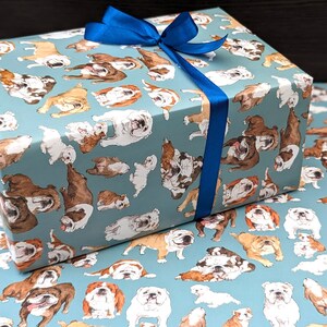 May include: Blue wrapping paper with a repeating pattern of brown and white bulldogs on a light blue background. A blue ribbon is tied around the box.