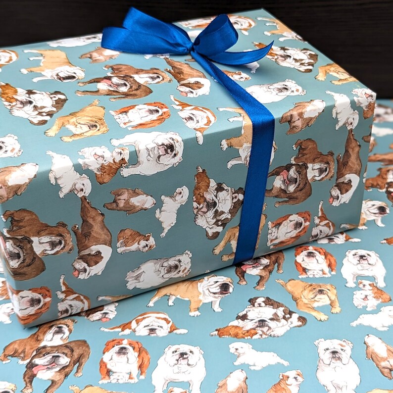 May include: Blue wrapping paper with a repeating pattern of brown and white bulldogs on a light blue background. A blue ribbon is tied around the box.
