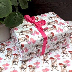 May include: A gift box wrapped in paper with a repeating pattern of a cartoon character, flowers, and pink hearts. The box is tied with a bright pink ribbon. The words "You are my precious" are printed on the wrapping paper.