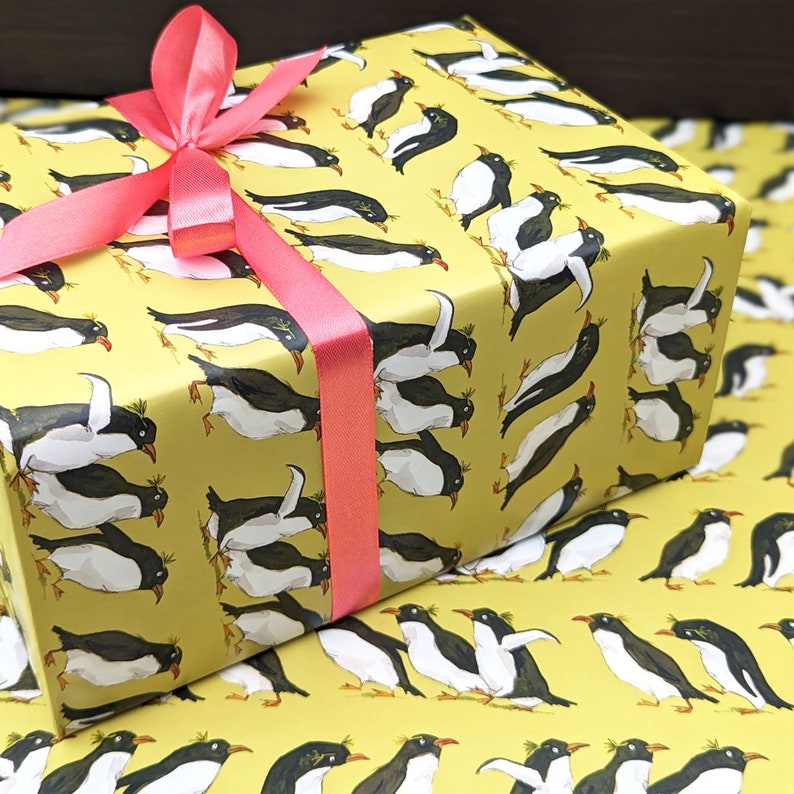Puede incluir: Papel de regalo amarillo con un patr&oacute;n repetitivo de ping&uuml;inos negros y blancos. El papel de regalo tiene una cinta rosa atada alrededor.