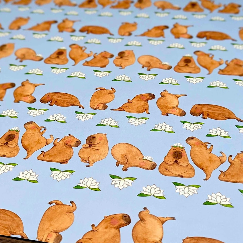 May include: A light blue background features a repeating pattern of brown capybaras in various yoga poses, interspersed with white lotus flowers. The capybaras are depicted in a cartoon style, with some wearing flower crowns.