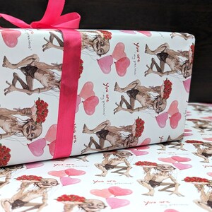 May include: Gift-wrapped present with white paper featuring a repeating pattern of a character holding flowers and heart-shaped balloons. The text "You are my precious" is also printed on the paper. A bright pink ribbon is tied around the gift.