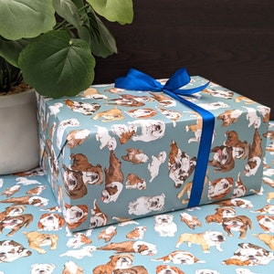May include: A blue gift box with a blue ribbon wrapped around it. The box is covered in a pattern of brown and white bulldogs.