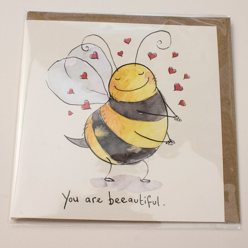 Op de afbeelding: Een aquarel-illustratie van een cartoon-bij met een glimlachend gezicht en vleugels. De bij is omringd door kleine rode hartjes. De tekst "You are bee-autiful." staat onder de bij.