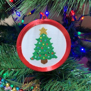 以下が含まれることがあります： 白地に緑色の刺繍でクリスマスツリーが施された、赤と白のクリスマスオーナメント