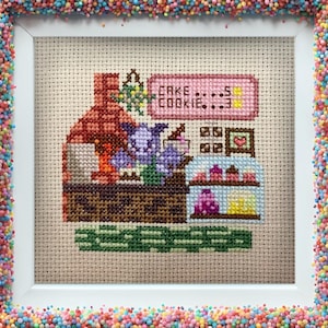 Puede incluir: Bordado de punto de cruz de una criatura morada de pie detrás de un mostrador con un letrero que dice "Cake & Cookie". El mostrador tiene una vitrina con pasteles y un horno de ladrillo en el fondo.