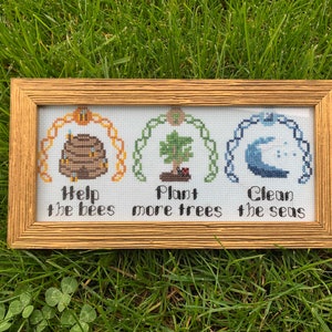 以下が含まれることがあります： 金色のフレームに入ったクロスステッチのアートワーク。デザインは、「Help the bees」、「Plant more trees」、「Clean the seas」というフレーズが書かれた3つのアーチ型のセクションが特徴です。各セクションには、蜂の巣、木、波の対応する画像があります。