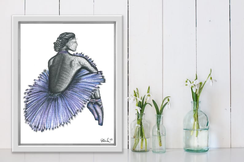 May include: A framed pencil drawing of a ballerina in a blue tutu, seated with her back to the viewer. The artwork is in a white frame, with a signature in the lower right corner. The background is white.