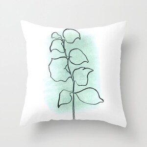 May include: A throw pillow with a minimalist line drawing of a plant with green watercolor wash in the background.