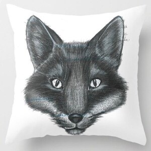 May include: A white square throw pillow featuring a detailed pencil drawing of a fox's face. The fox is depicted in shades of gray and black, with bright white eyes and a fluffy appearance. The pillow is a decorative item.