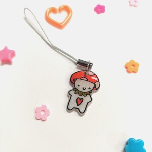 May include: A whimsical mushroom charm with a red cap and a smiling face, attached to a silver-colored lanyard. The charm features a heart on its chest. Scattered around are various colorful plastic shapes, including stars, hearts, and flowers.