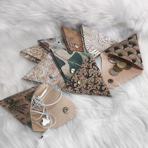 Könnte beinhalten: Eine Sammlung dreieckiger Beutel in verschiedenen Mustern und Farben, darunter Blumen-, Anker- und geometrische Designs. Einige Beutel sind geöffnet und zeigen Münzen und Ohrhörer. Die Beutel sind aus Stoff und haben Druckknöpfe.