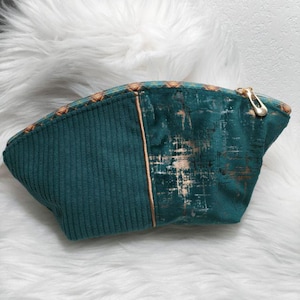 May include: Teal corduroy and textured cosmetic bag with a gold zipper. The bag features a vertical gold accent and a patterned top edge. The textured side has a gold distressed pattern.