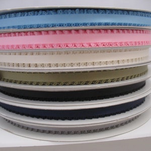 May include: A stack of spools of ribbon with scalloped edges in various colors, including light blue, pink, cream, khaki, black, navy, and gray.