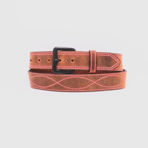 May include: A brown leather belt featuring bright pink stitching in a repeating wave pattern along the length of the strap. The belt includes a matte black metal buckle and a matching leather keeper loop, with visible adjustment holes.