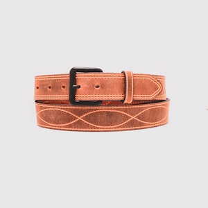 May include: A tan leather belt featuring a matte black buckle and a repeating stitched wave pattern along the strap. The belt includes a matching leather keeper loop and visible orange contrast stitching throughout the entire length of the strap.