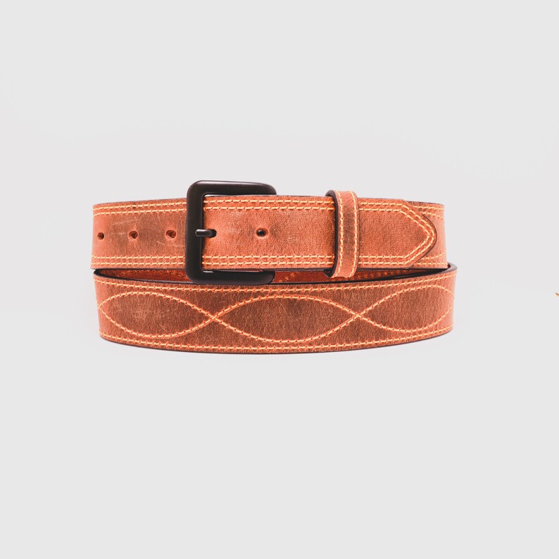 May include: A tan leather belt featuring a matte black buckle and a repeating stitched wave pattern along the strap. The belt includes a matching leather keeper loop and visible orange contrast stitching throughout the entire length of the strap.