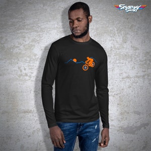 May include: A black long-sleeve t-shirt with an orange silhouette of a person riding a bicycle over a blue mountain range with an orange sun in the background.