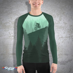 May include: A green long-sleeve shirt with a forest scene and a silhouette of a person riding a mountain bike on a trail.