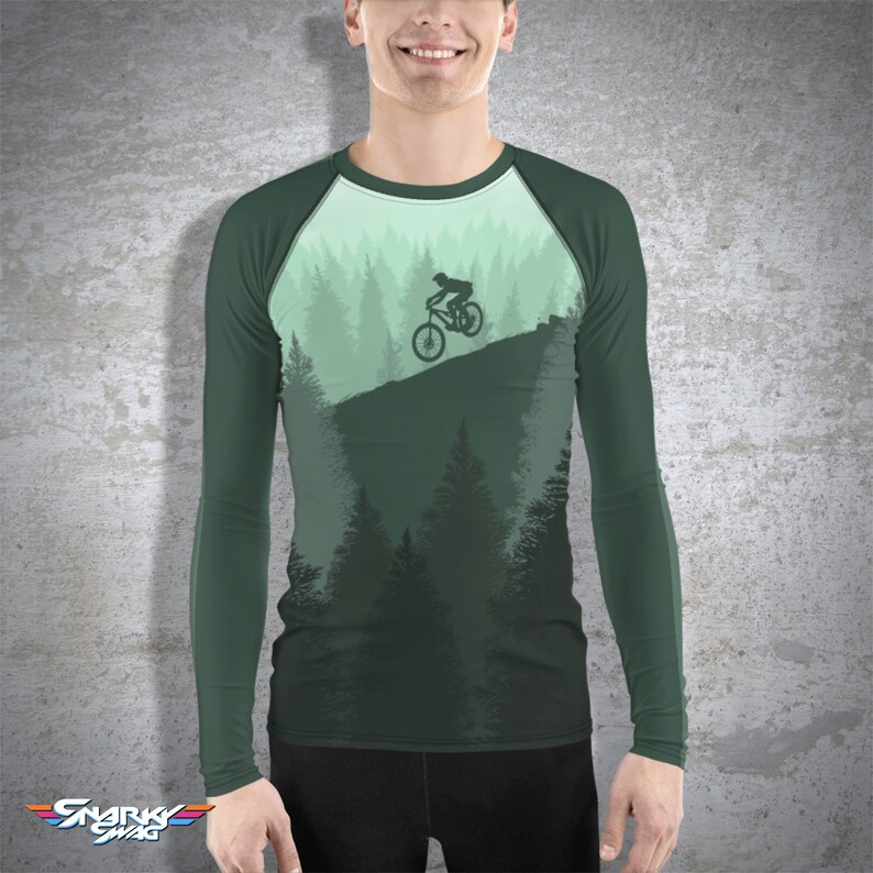 May include: A green long-sleeve shirt with a forest scene and a silhouette of a person riding a mountain bike on a trail.