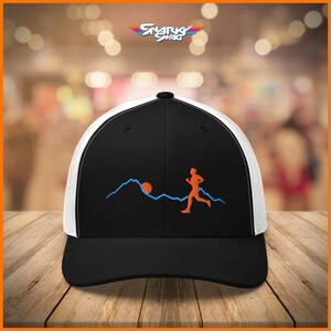 Puede incluir: Gorra de camionero negra y blanca con un dise&ntilde;o bordado en negro de una persona corriendo por una cordillera con el sol saliendo detr&aacute;s de ella. El dise&ntilde;o es en naranja y azul.