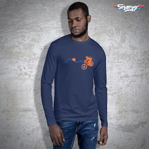 May include: A navy blue long-sleeve t-shirt with a graphic of a person riding a mountain bike over a mountain range with a setting sun. The text "SNARKY SWAG" is in the upper right corner of the image.
