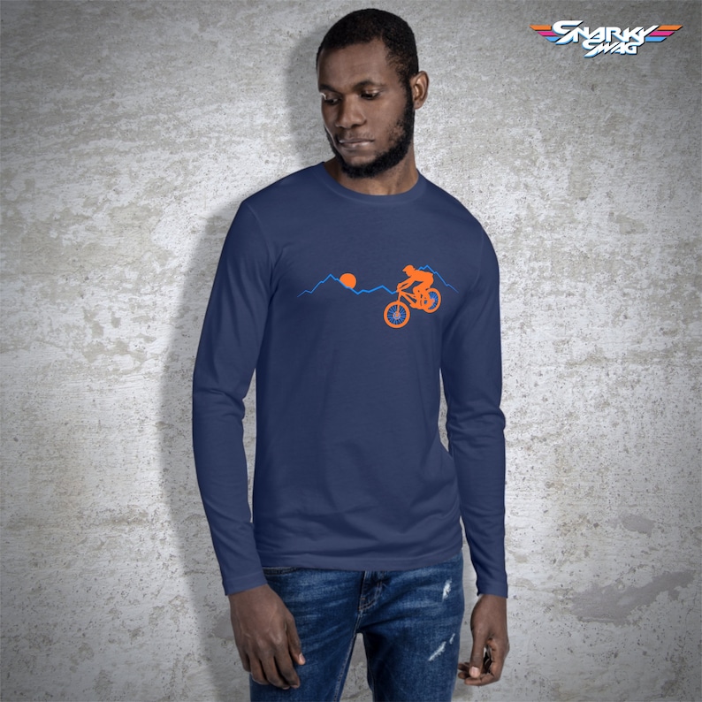 May include: A navy blue long-sleeve t-shirt with a graphic of a person riding a mountain bike over a mountain range with a setting sun. The text "SNARKY SWAG" is in the upper right corner of the image.