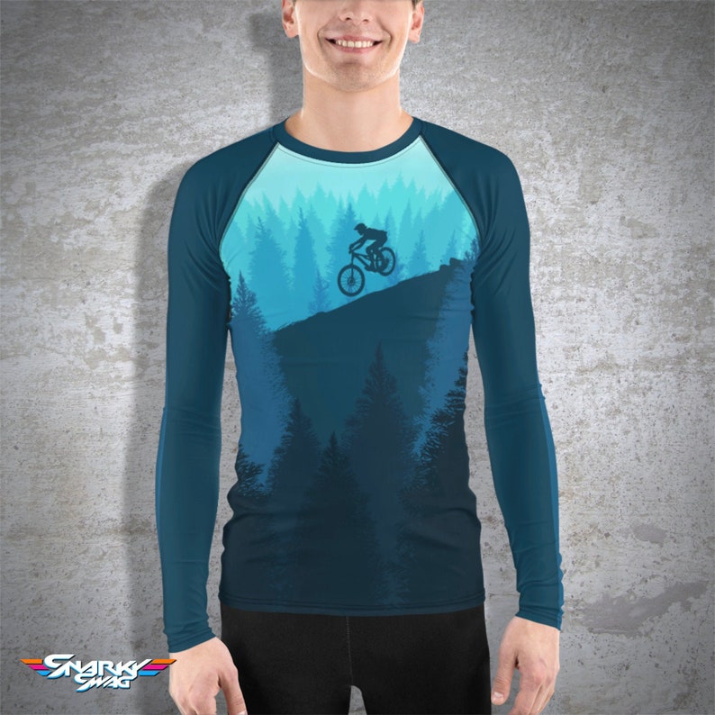 May include: A long-sleeved shirt with a blue and teal design featuring a silhouette of a person riding a mountain bike through a forest.